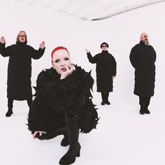 a woman with red hair sitting on the ground in front of other people wearing black clothing