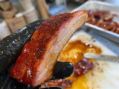 a person holding up a piece of meat in front of some other food on the table