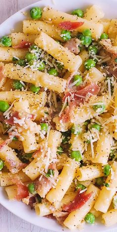 a white bowl filled with pasta, peas and cheese on top of a wooden table