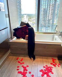 a woman with long black hair sitting in a bathtub surrounded by red rose petals