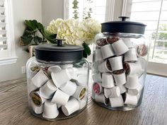 two glass jars filled with different types of buttons on top of a wooden table next to a window