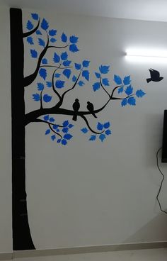 two birds sitting on a tree branch with blue leaves painted on the wall behind it