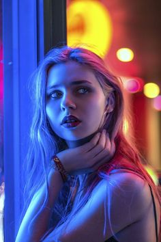 a woman with long blonde hair and red lipstick posing in front of a window at night