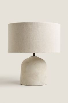 a white table lamp with a beige shade on the base and a light bulb attached to it