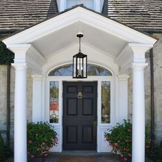 a black front door with white pillars and flowers