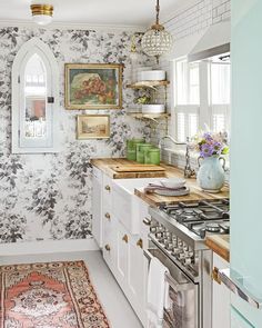 a white kitchen with floral wallpaper and an ornate rug on the floor next to the stove