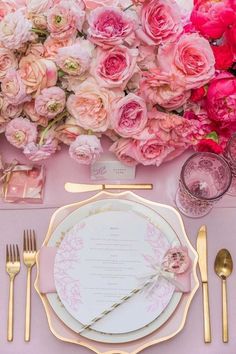 a table set with pink flowers and gold place settings