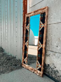 an old mirror leaning against a wall next to a cement building with a blue sky in the background