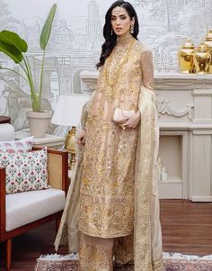 a woman standing in front of a fireplace wearing a gold dress and matching shawl