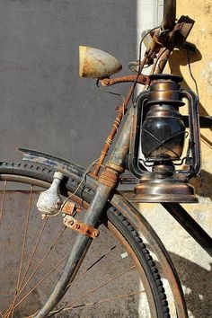 an old rusty bicycle with a lantern on the handlebars is parked in front of a building