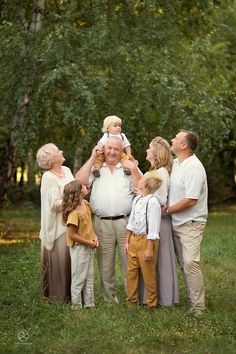 an older man holding a baby while standing between two adults and three children in front of trees