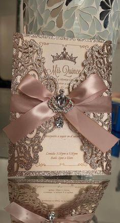 the wedding card is decorated with pink ribbon and a jeweled brooch on top