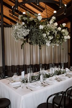 a long table is set with white flowers and place settings for the dinner guests to sit at