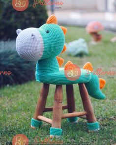 a crocheted toy dinosaur sitting on top of a wooden stool in the grass