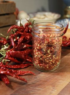 some red peppers are sitting on a wooden cutting board next to a jar of chili seasoning