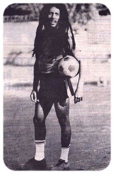 a man with dreadlocks holding a soccer ball in his right hand and wearing socks