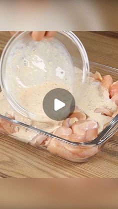 a person pouring dressing into a glass dish on a wooden table with chicken in it