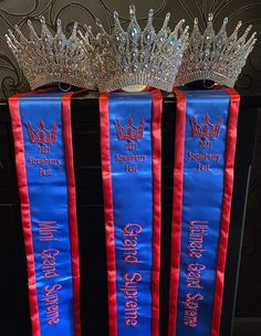 two blue sashs with silver crowns on top of each one and red ribbon around the edges