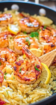 a skillet filled with pasta and shrimp, garnished with lemon wedges