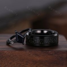 two wedding rings sitting on top of a wooden table next to each other, one with a black diamond in the center