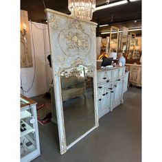 an old white cabinet with a mirror on top and people in the background looking at it