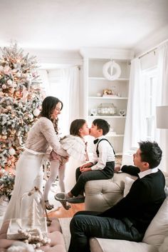 a family sitting in front of a christmas tree with the child kissing his mother's cheek