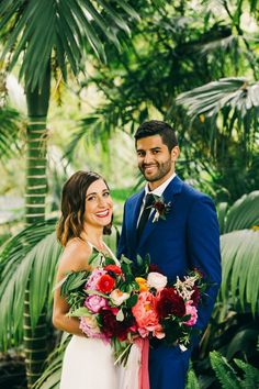 a man and woman standing next to each other in front of palm trees holding bouquets