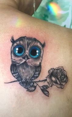 an owl with big blue eyes sitting on a branch next to a rose tattoo design