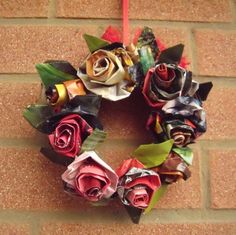 a wreath made out of rolled up paper flowers hanging on a brick wall with a red ribbon