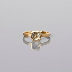 a yellow gold ring with a square cut diamond on the front and side, sitting on a reflective surface