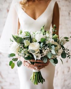 a bride holding a bouquet of white flowers and greenery