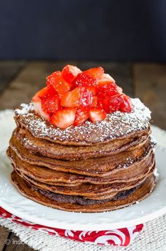 a stack of chocolate pancakes covered in powdered sugar and topped with strawberries