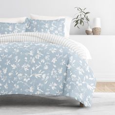 a bed with blue and white floral comforter set on it's side, next to a potted plant