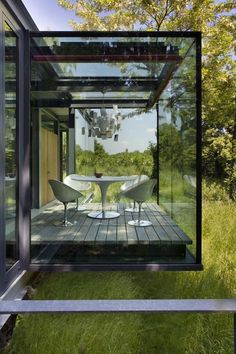 a glass house with tables and chairs in the middle of it, surrounded by green grass