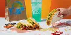 a person holding a taco in front of a bag and some chips on the table