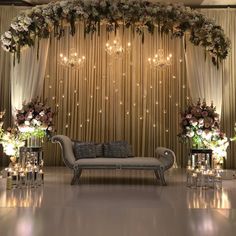 a couch sitting under a chandelier filled with flowers and candles in front of a curtain