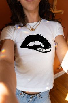 Introducing the Black Lip Baby Tee from PrintWithSky — your go-to piece for an effortless blend of style and comfort. Dazzle with this trendy Y2K-inspired top featuring a bold black lips graphic on a pristine white backdrop. Whether you're hitting the streets or just keeping it casual, this stylish streetwear top commands attention. It's designed to offer a perfect slim fit that accentuates your silhouette. Don't wait to add this must-have tee to your wardrobe. The model is wearing an XS size. O Kendall White, Outfit Ideas Grunge, Minimal Shirt Design, Tops For Women Casual, Trendy Shirt Designs, Workout Tops For Women, Baby Graphic Tees, Black Lips, Streetwear Tops