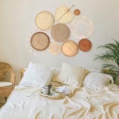 a bed with white linens and woven baskets on the wall above it, next to a wicker chair