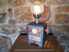 an old fashioned stove lamp sitting on top of a table next to a stone wall