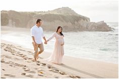 a pregnant couple walking on the beach holding hands