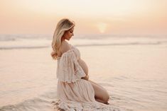 a pregnant woman sitting on top of a surfboard in the ocean at sunset or sunrise