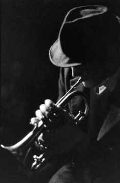 black and white photograph of a man with a trumpet in his hand, wearing a hat