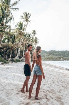 a man and woman standing on the beach next to each other with palm trees in the background