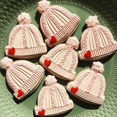 six decorated cookies in the shape of hats on a green platter with red hearts