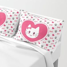 a bed with two pillows on top of it and a cat in a heart shaped frame