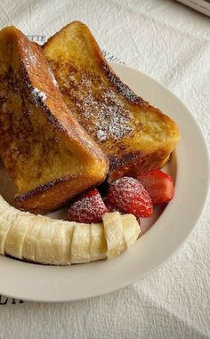 two pieces of french toast on a white plate with strawberries and bananas next to it