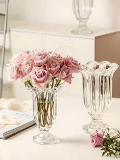 two clear vases with pink roses in them on a white table next to a mirror