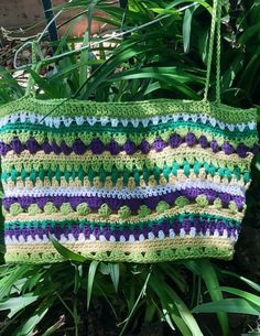 a crocheted bag hanging from a tree in front of some leaves and plants