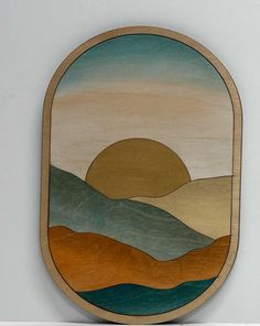 a wooden plaque with an image of mountains and the sun in the sky on it