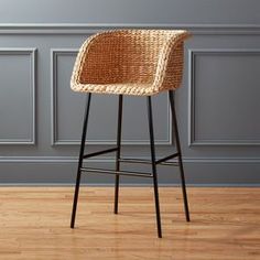 a wicker bar stool in front of a gray wall and wood flooring with a black metal frame